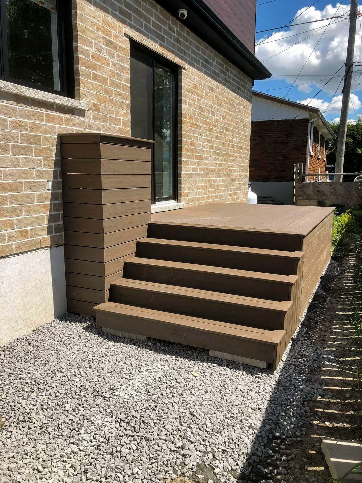 Une terrasse en bois avec des escaliers menant à une maison en briques.