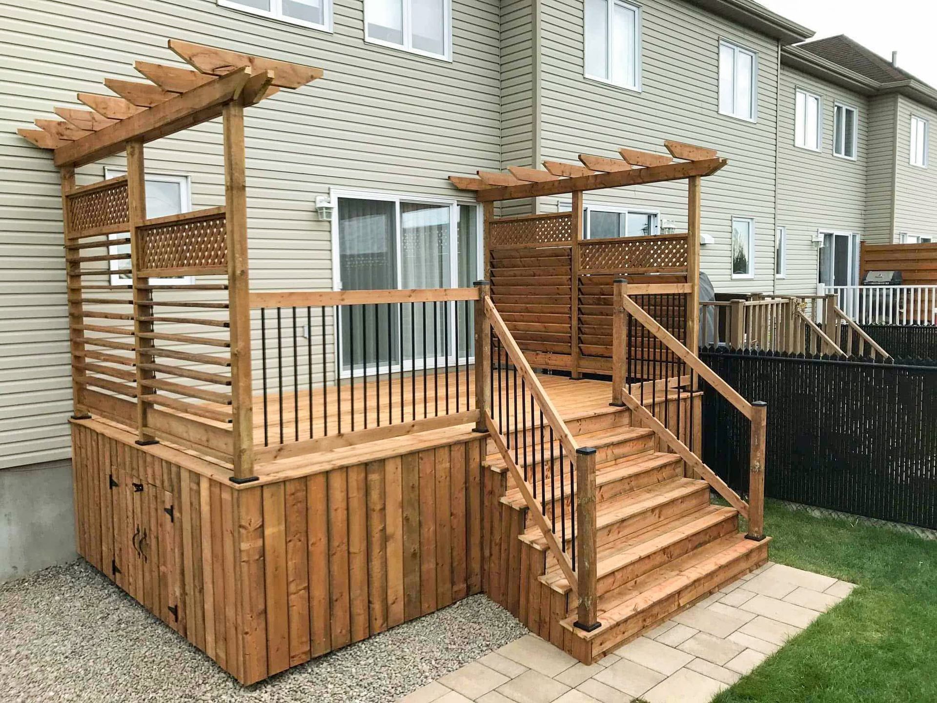 Une terrasse en bois avec des escaliers et une pergola devant une maison.