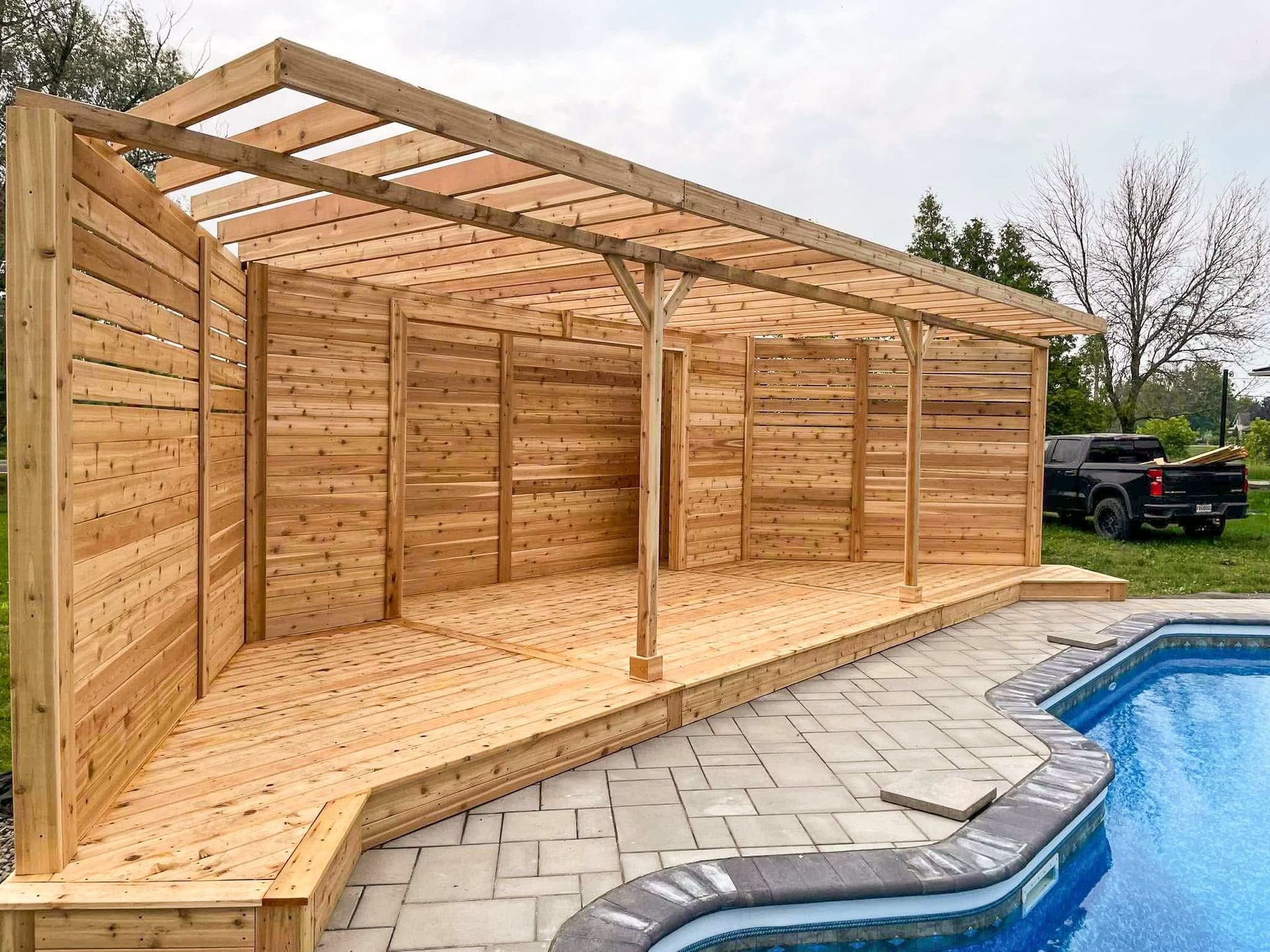 Une structure en bois est assise à côté d'une piscine.