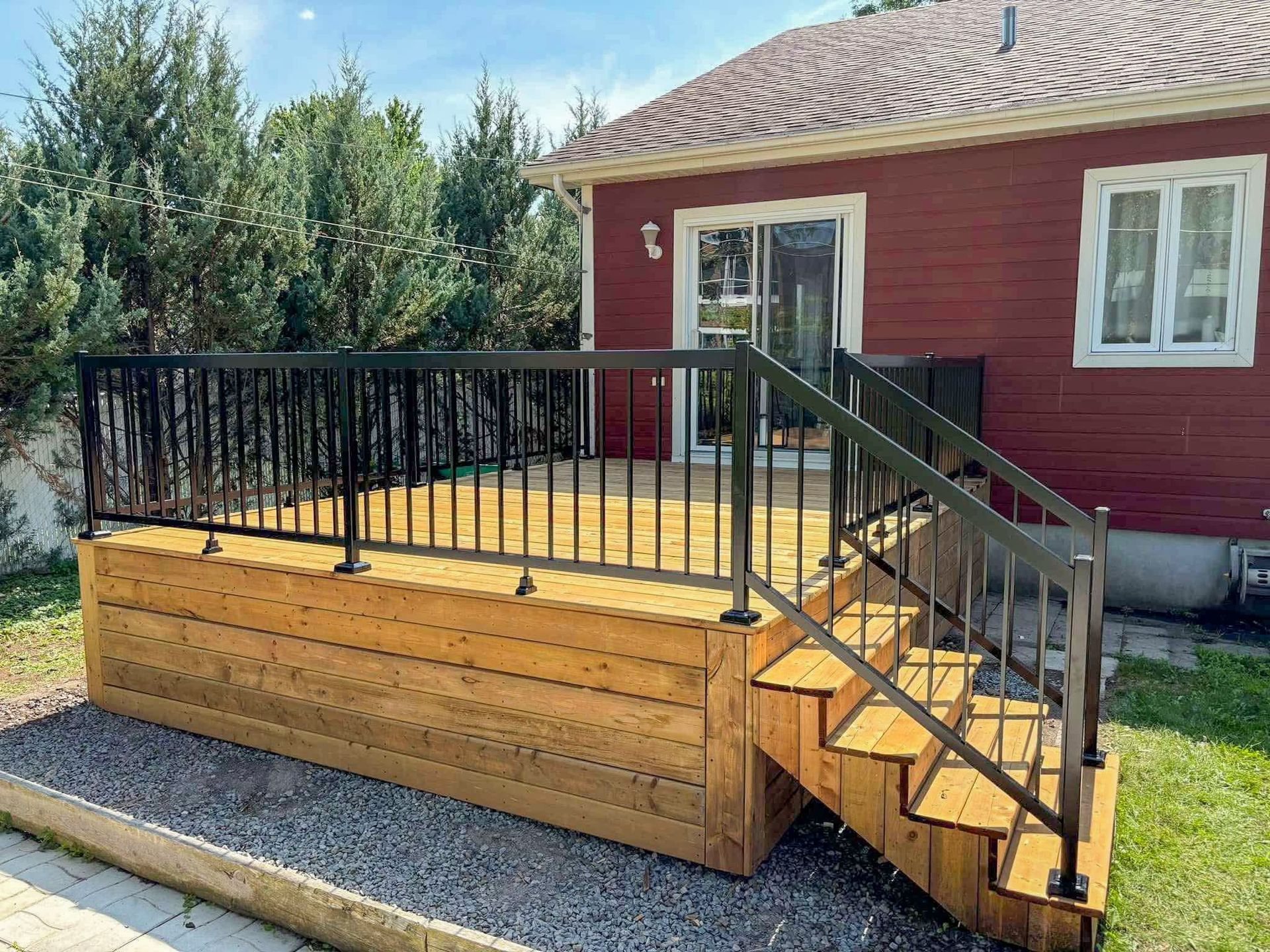 Une terrasse en bois avec des escaliers et une balustrade en métal devant une maison rouge.