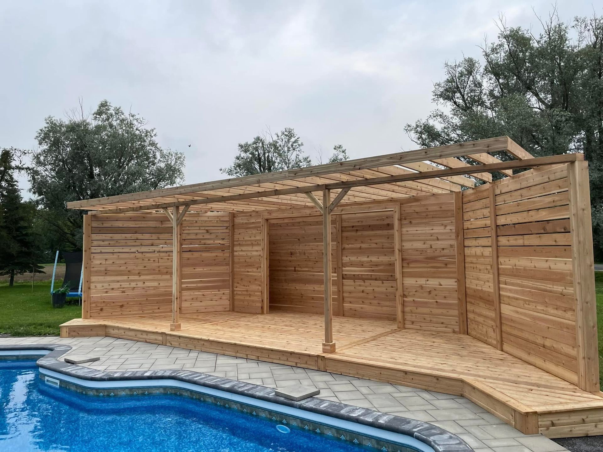 Une structure en bois est assise à côté d'une piscine.