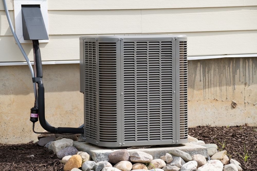 An air conditioner is sitting outside of a house next to a pile of rocks.