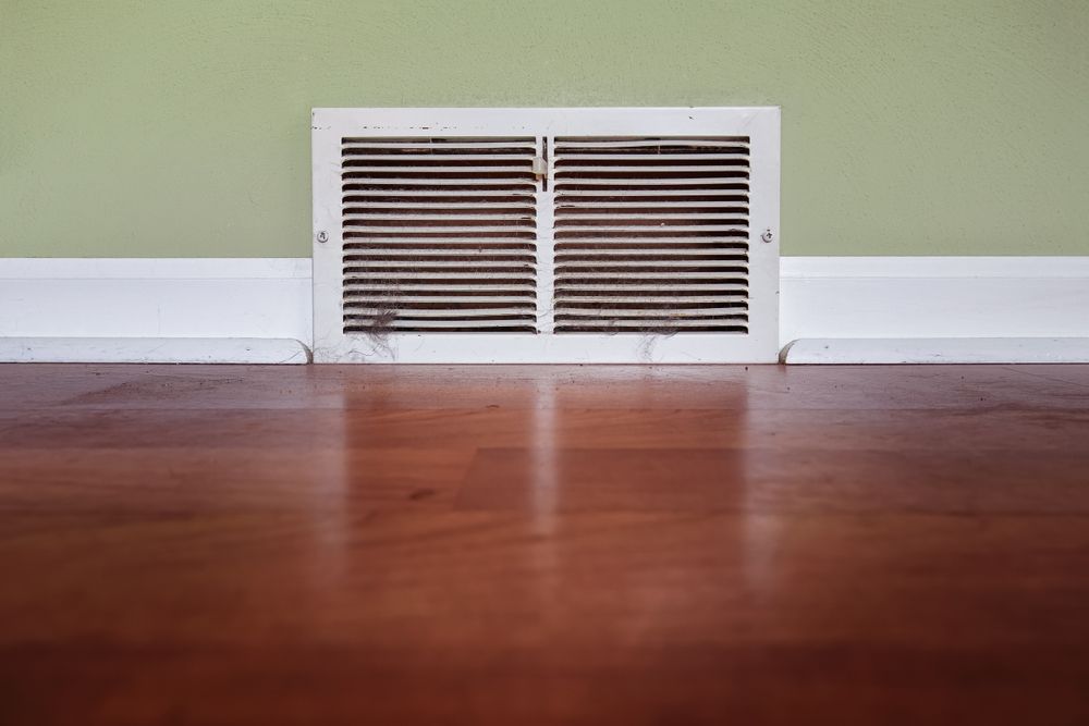 An air vent on the floor of a room with a green wall.