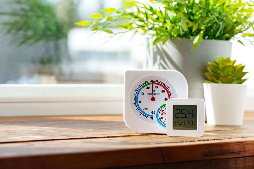 A clock and a thermometer are sitting on a wooden table.