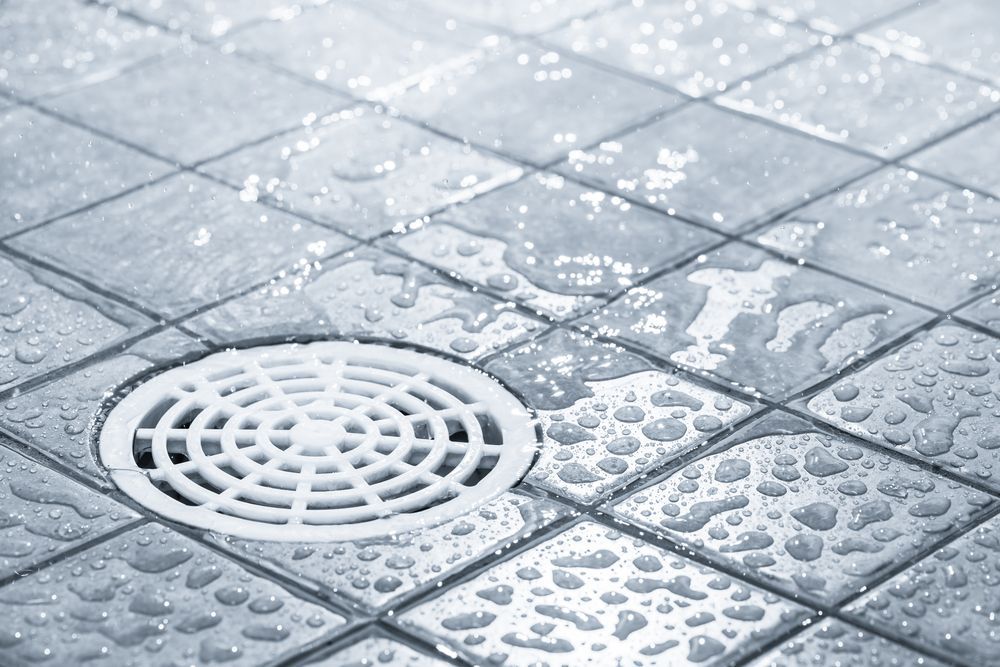 A drain on a tiled floor with water drops on it.