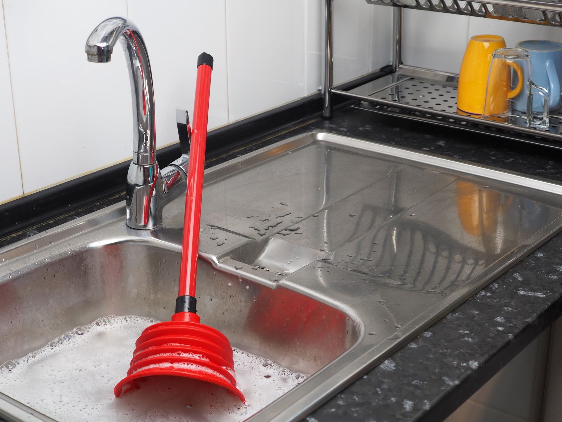 A kitchen sink with a red plunger in it