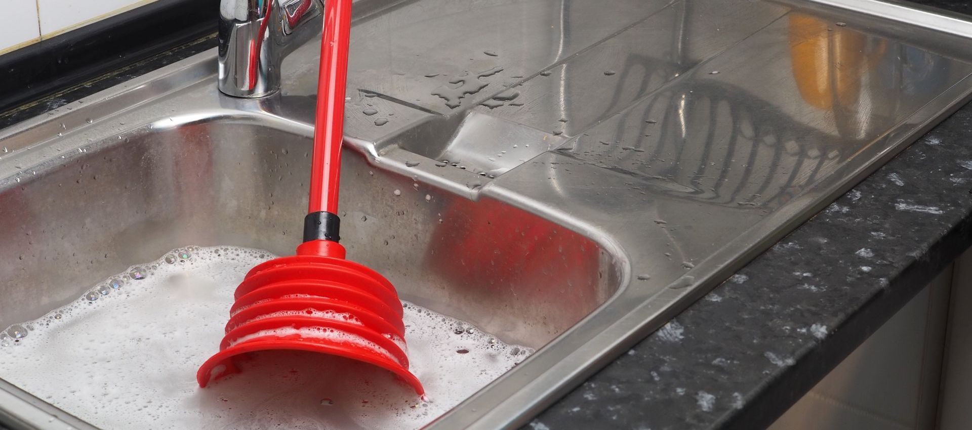 A kitchen sink with a red plunger in it