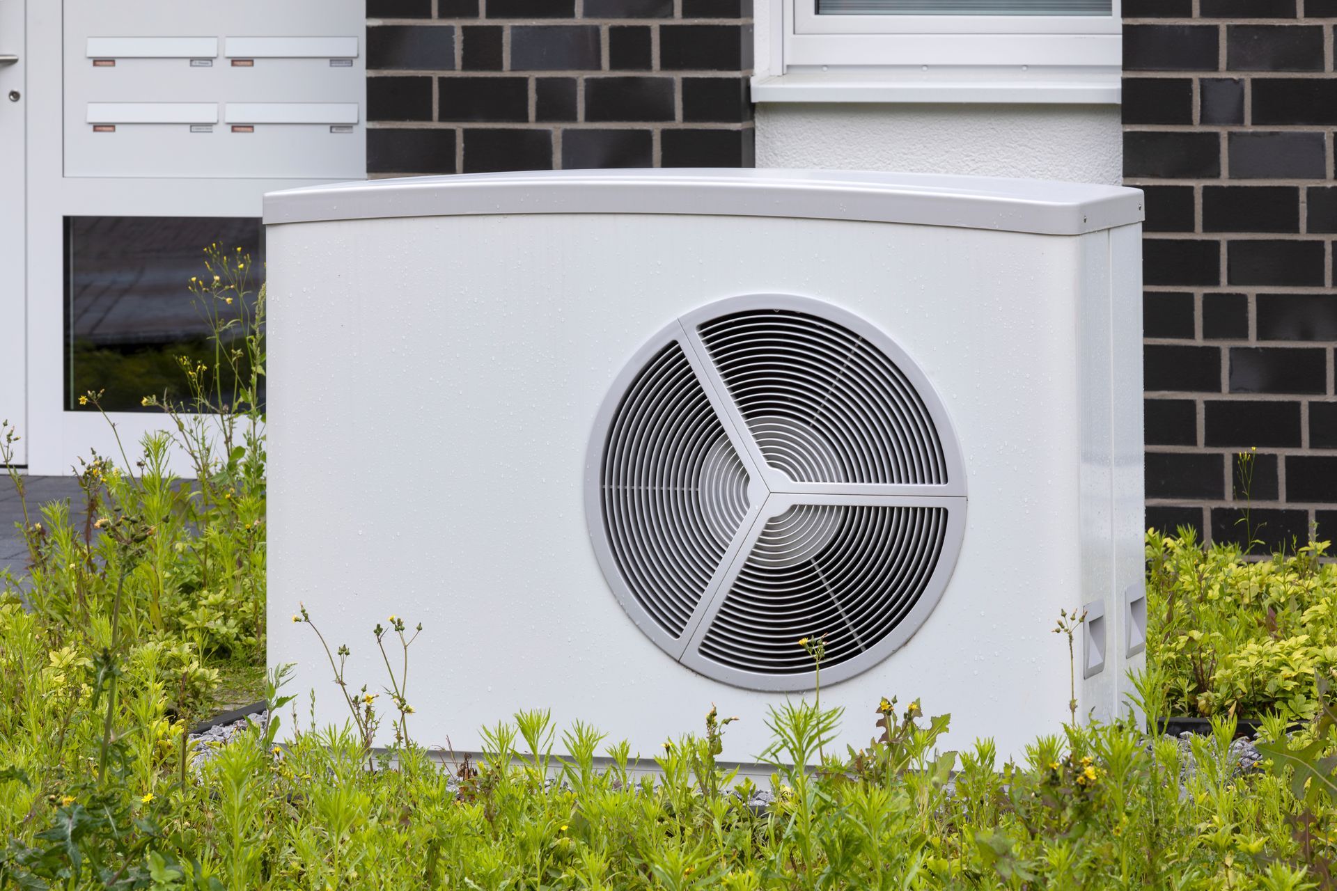 A white air conditioner is sitting in front of a brick building.