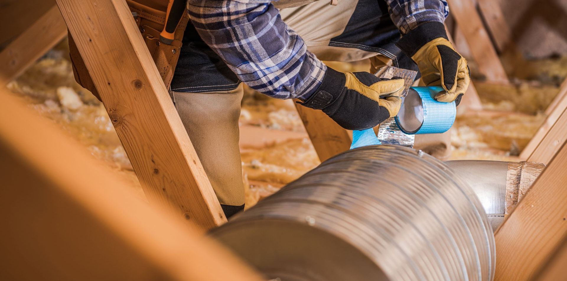 A man is working on a duct in the attic of a house.