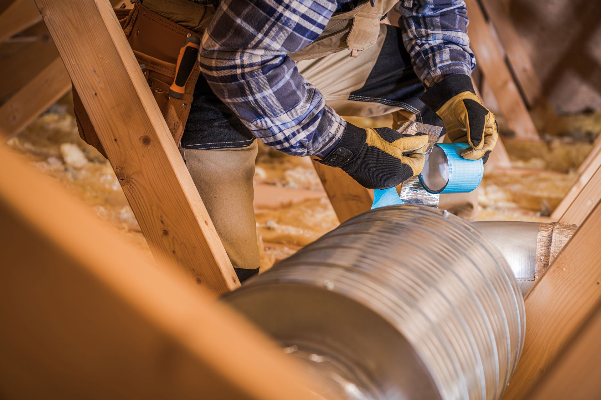 A man is working on a duct in the attic of a house.