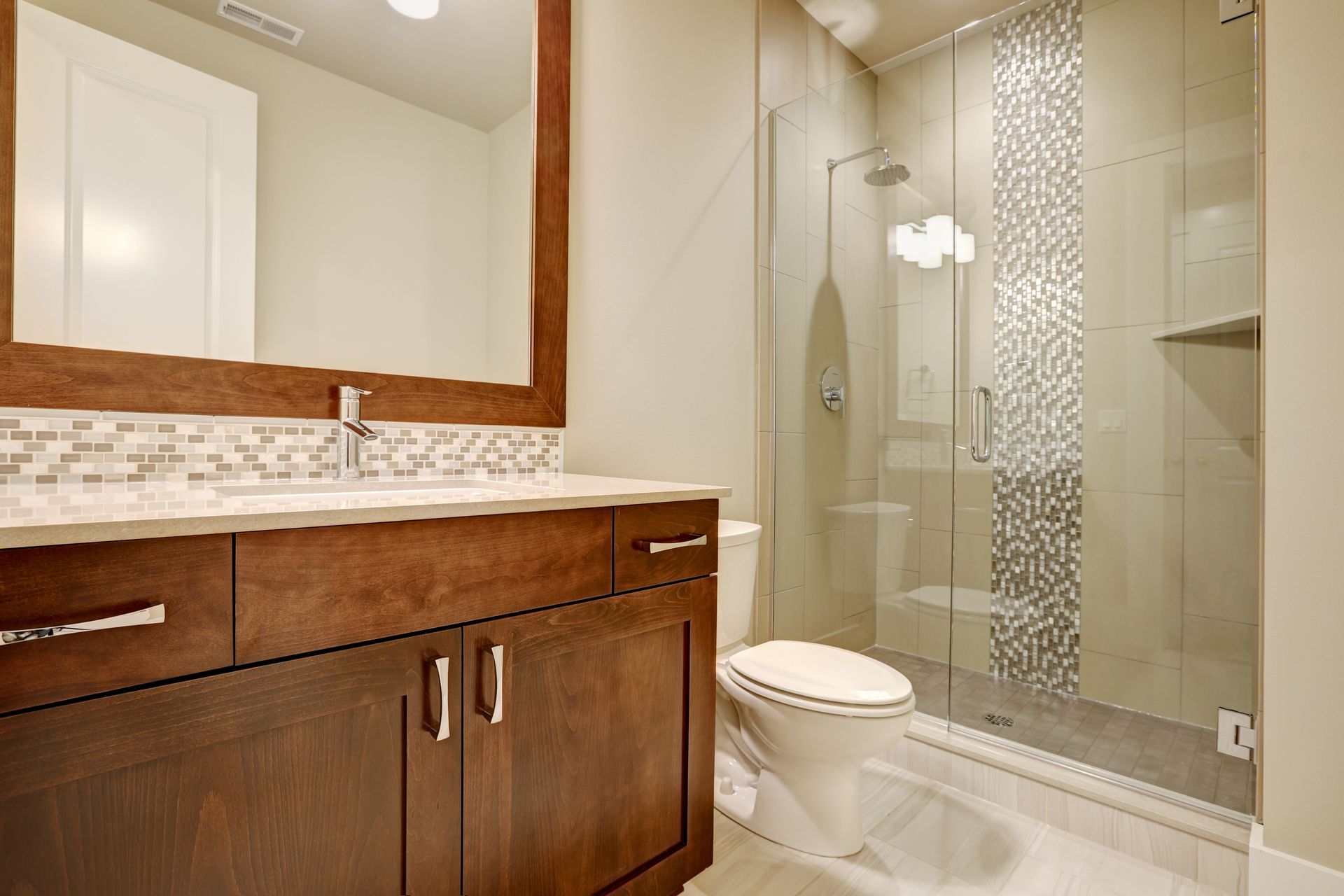 Bathroom with a dark wooden vanity, glass shower, and a mosaic accent tile.