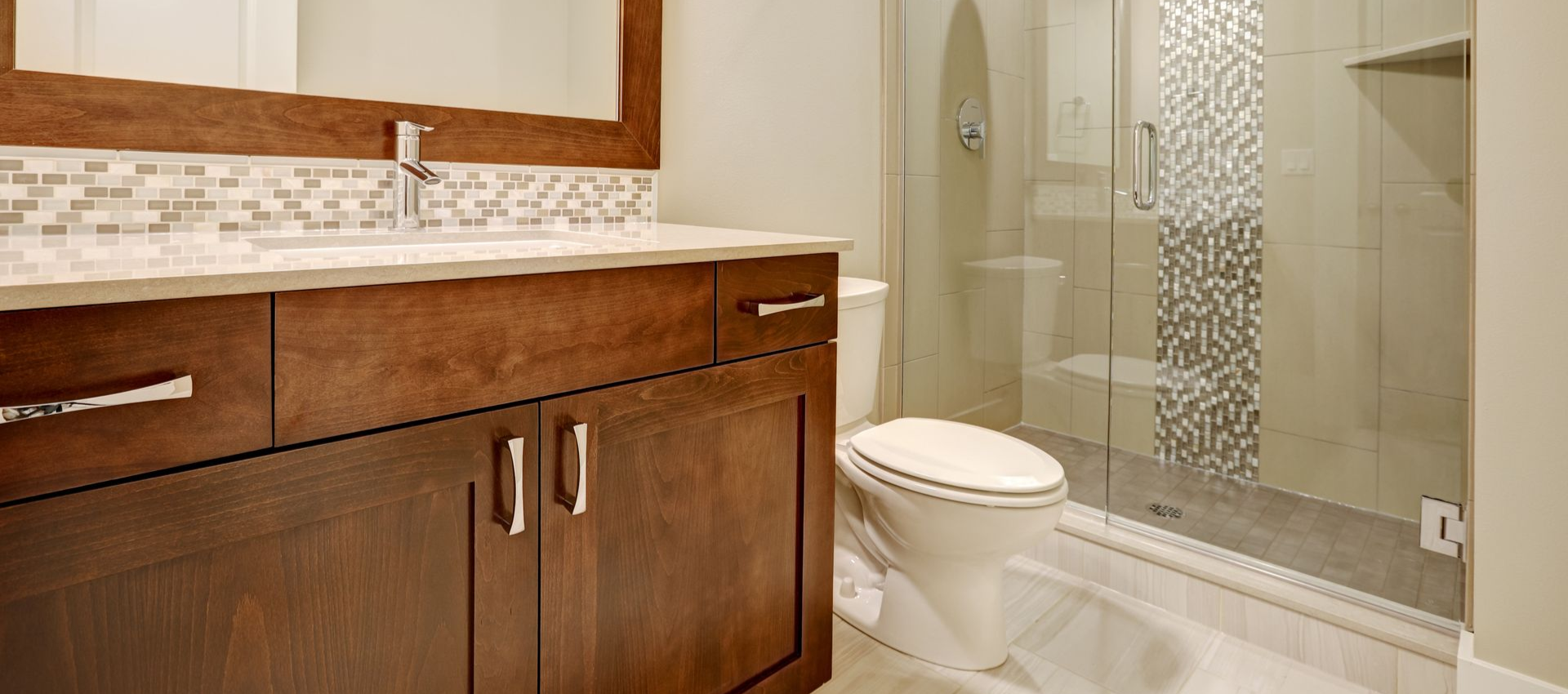 Bathroom with dark wood vanity, white countertop, glass shower, and mosaic tile accent.