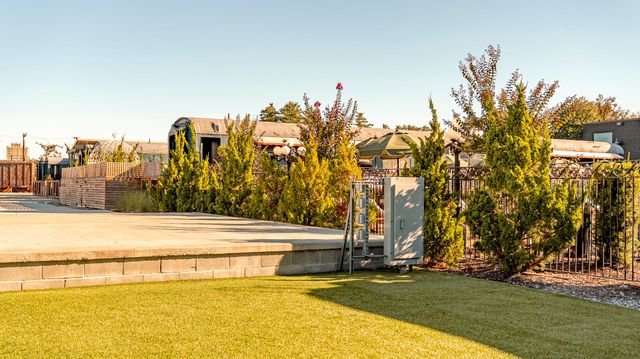 A level concrete area with a grassy lawn, trees, and buildings in the background.