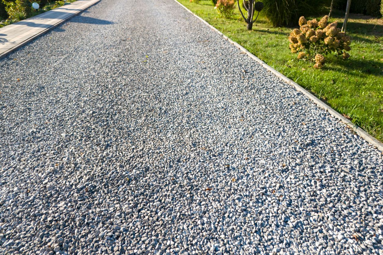 Gravel driveway bordered by concrete and green grass. Sunny outdoor setting.