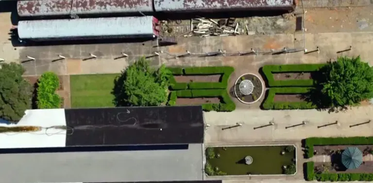 Aerial view of a garden with a fountain, manicured hedges, and a water feature next to train cars.