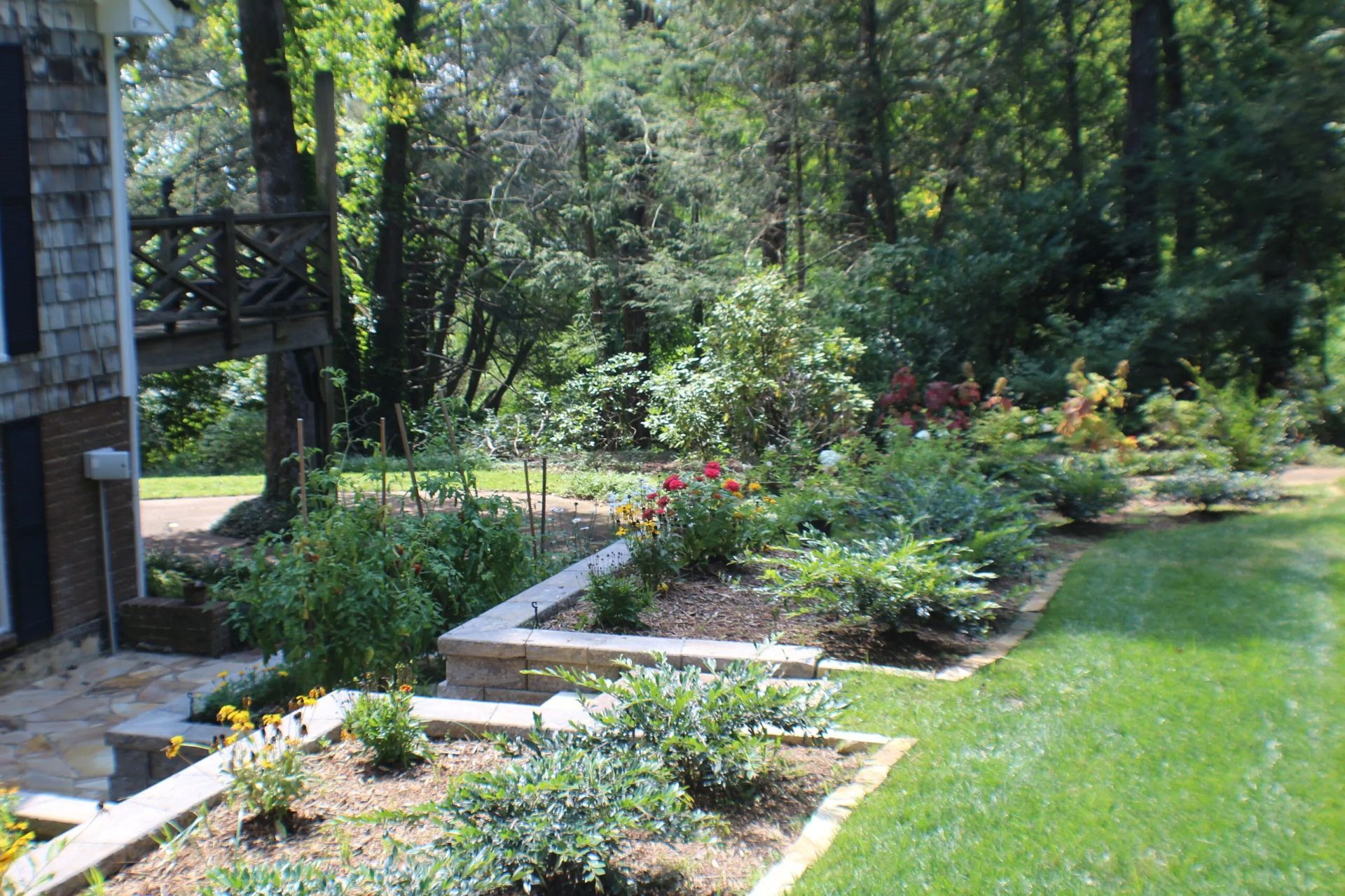 Garden bed with brick edging next to a house and lawn, surrounded by trees.