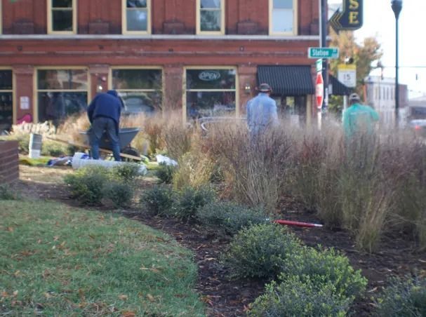 People tending to landscaping in front of a brick building.