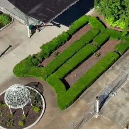 Aerial view of a garden with a hedge maze and a decorative white gazebo on a concrete surface.