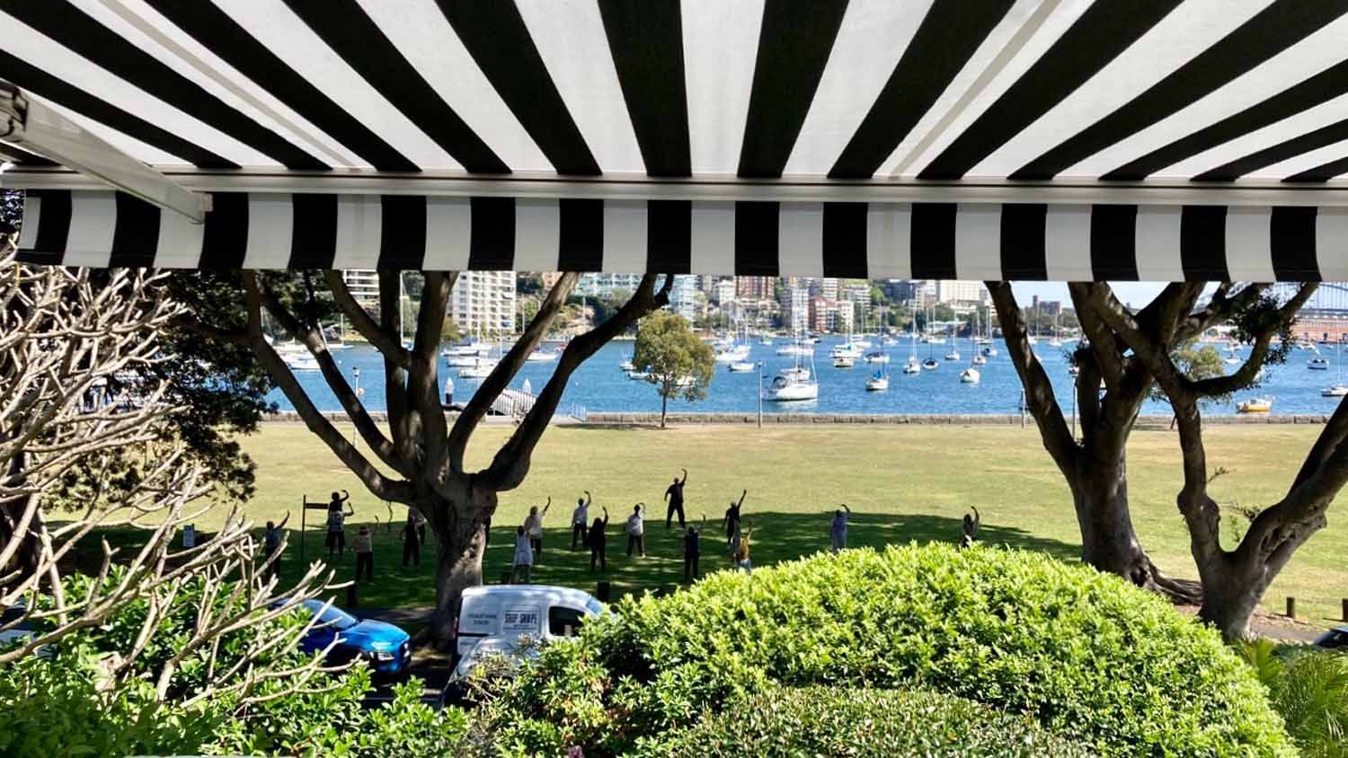 A black and white striped awning over a grassy area with a body of water | Sydney, NSW | Sunmaster Australia