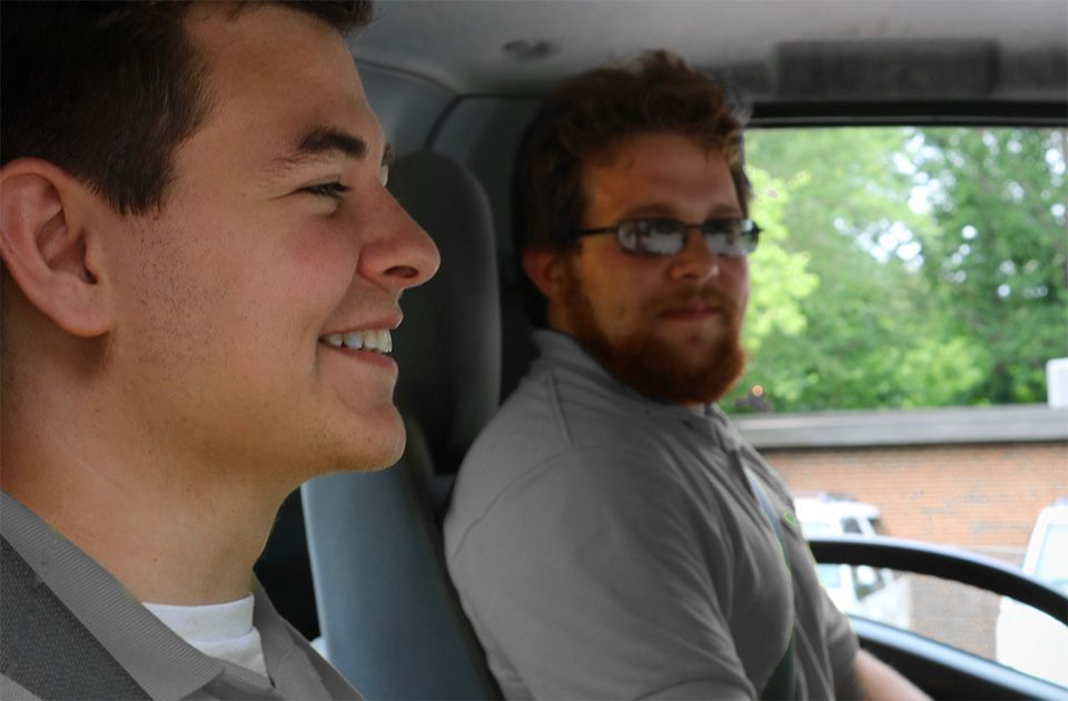 Two men are sitting in a car and one is smiling