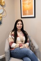 A woman is sitting on a couch with her legs crossed and smiling.