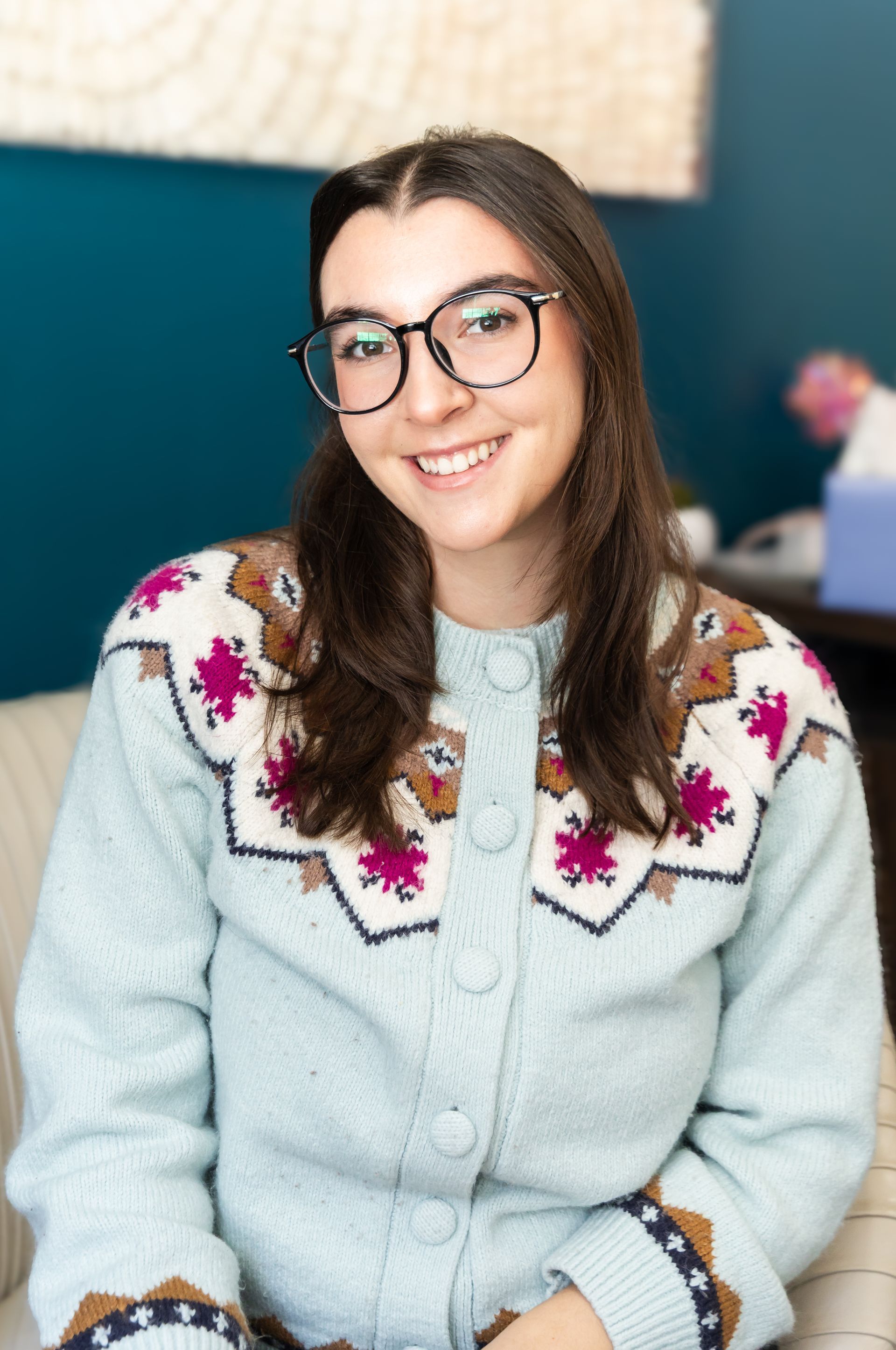 A man in a suit and glasses is sitting in a chair in front of a window.