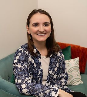 A woman is sitting on a couch with pillows and smiling for the camera.
