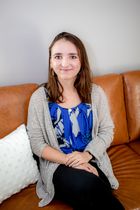 A woman is sitting on a couch with her legs crossed and smiling.