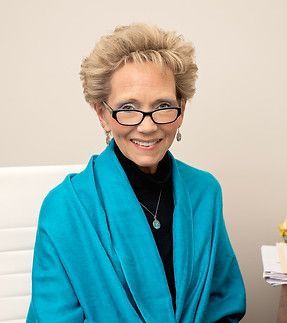 A woman wearing glasses and a blue scarf is sitting in a chair.