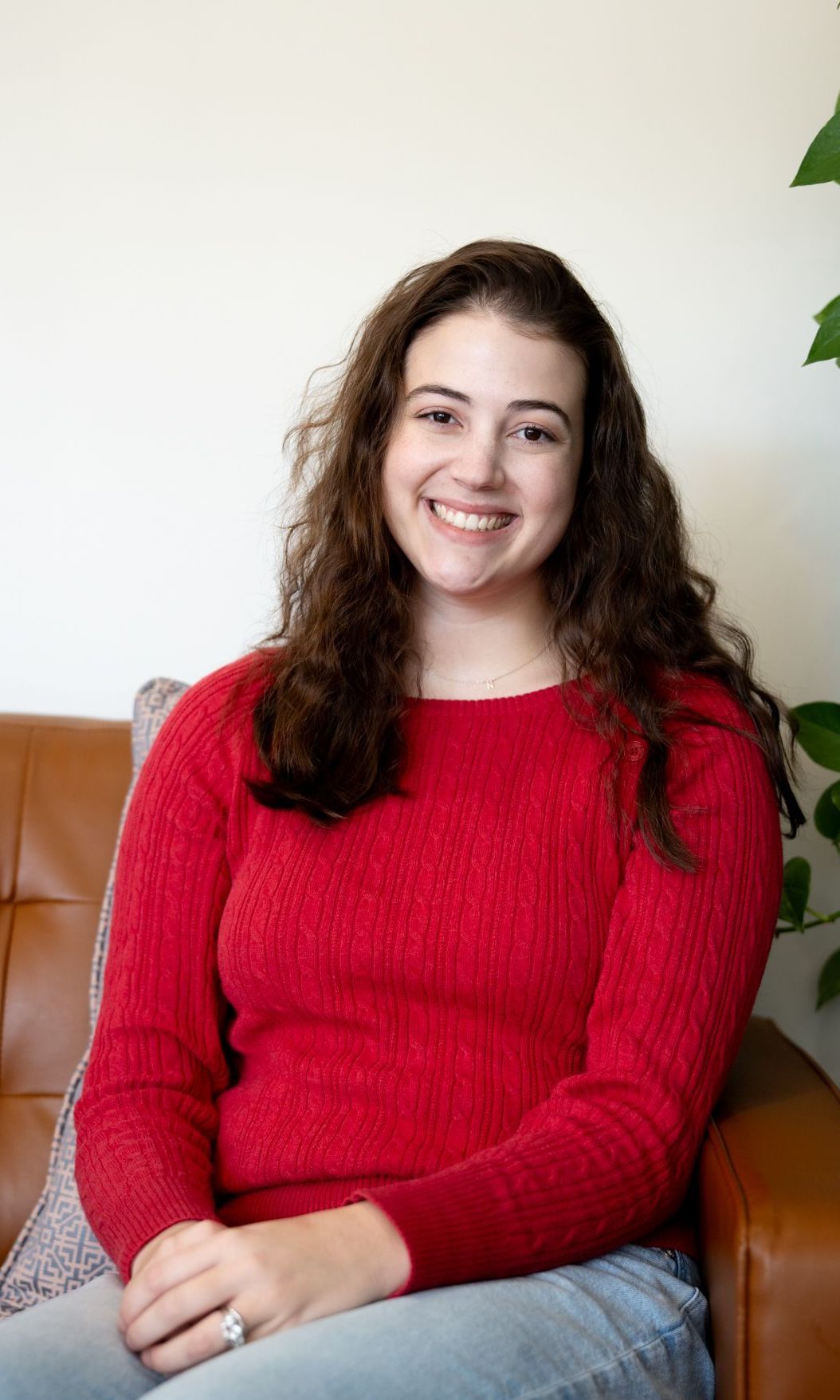 A woman is sitting on a couch with pillows and smiling for the camera.