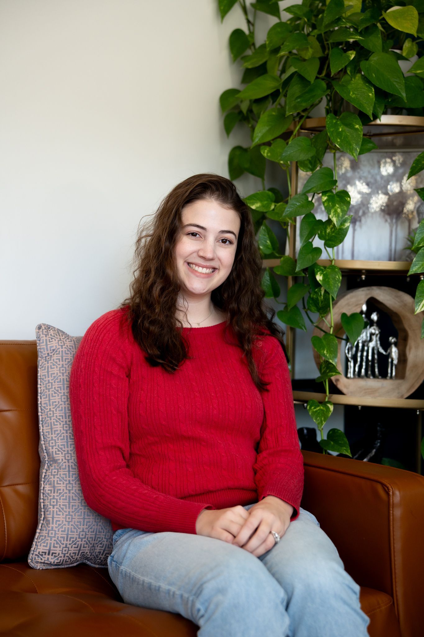 A woman is sitting on a couch with pillows and smiling for the camera.