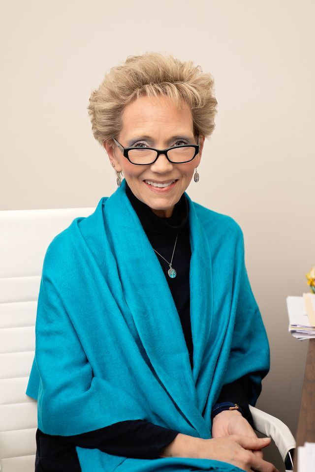 A woman wearing glasses and a blue scarf is sitting in a chair.