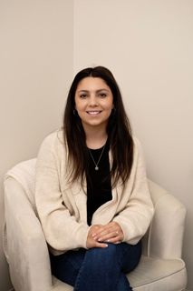 A woman is sitting in a chair with her legs crossed and smiling.