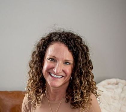 A woman is sitting on a couch with pillows and smiling for the camera.