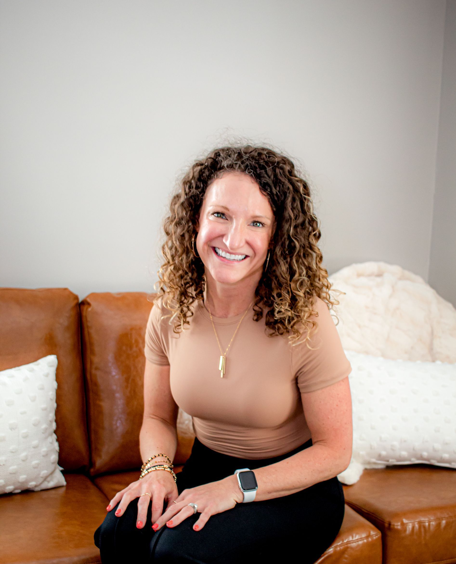 A woman is sitting on a couch with pillows and smiling for the camera.