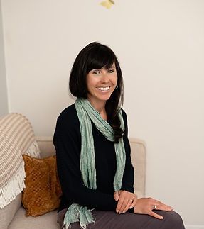 A woman is sitting on a couch wearing a scarf and smiling.