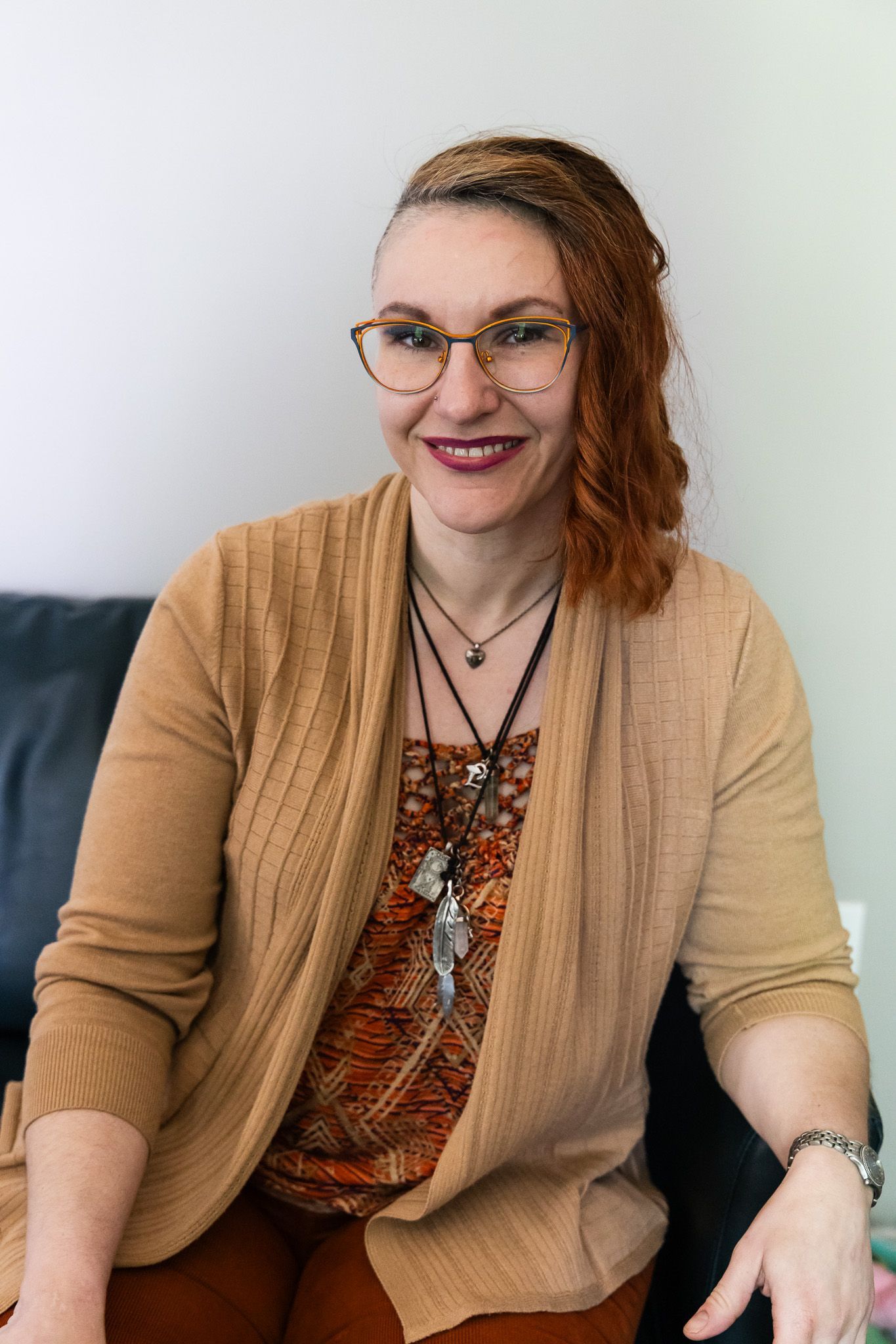 A woman is sitting on a couch with her legs crossed and smiling.
