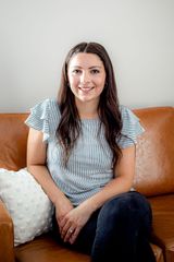 A woman is sitting on a couch wearing a black turtleneck sweater.
