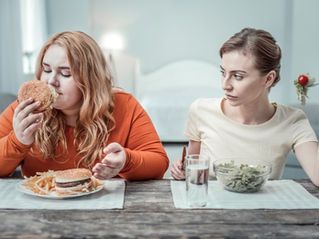 Two women are sitting at a table eating hamburgers and french fries.