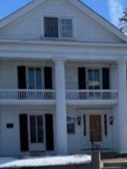 A large white house with black shutters and a balcony.