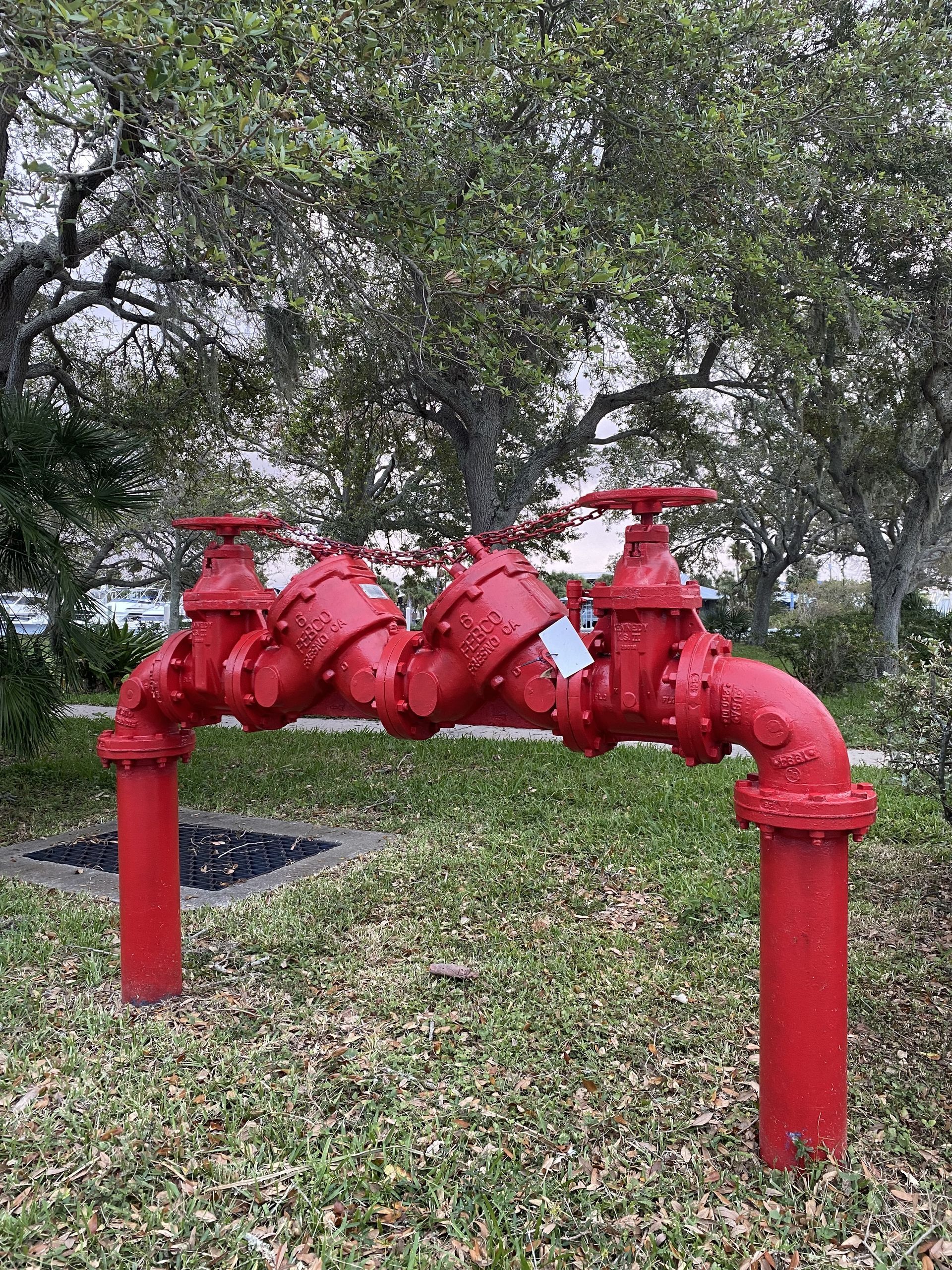 Red water pipes with valves in a park, against trees.