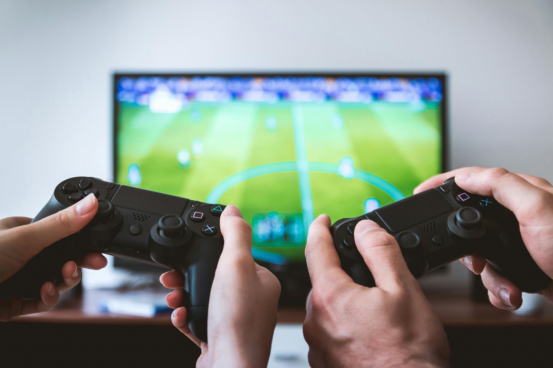 Two people playing a video game together, holding black controllers in front of a TV screen showing a soccer game.