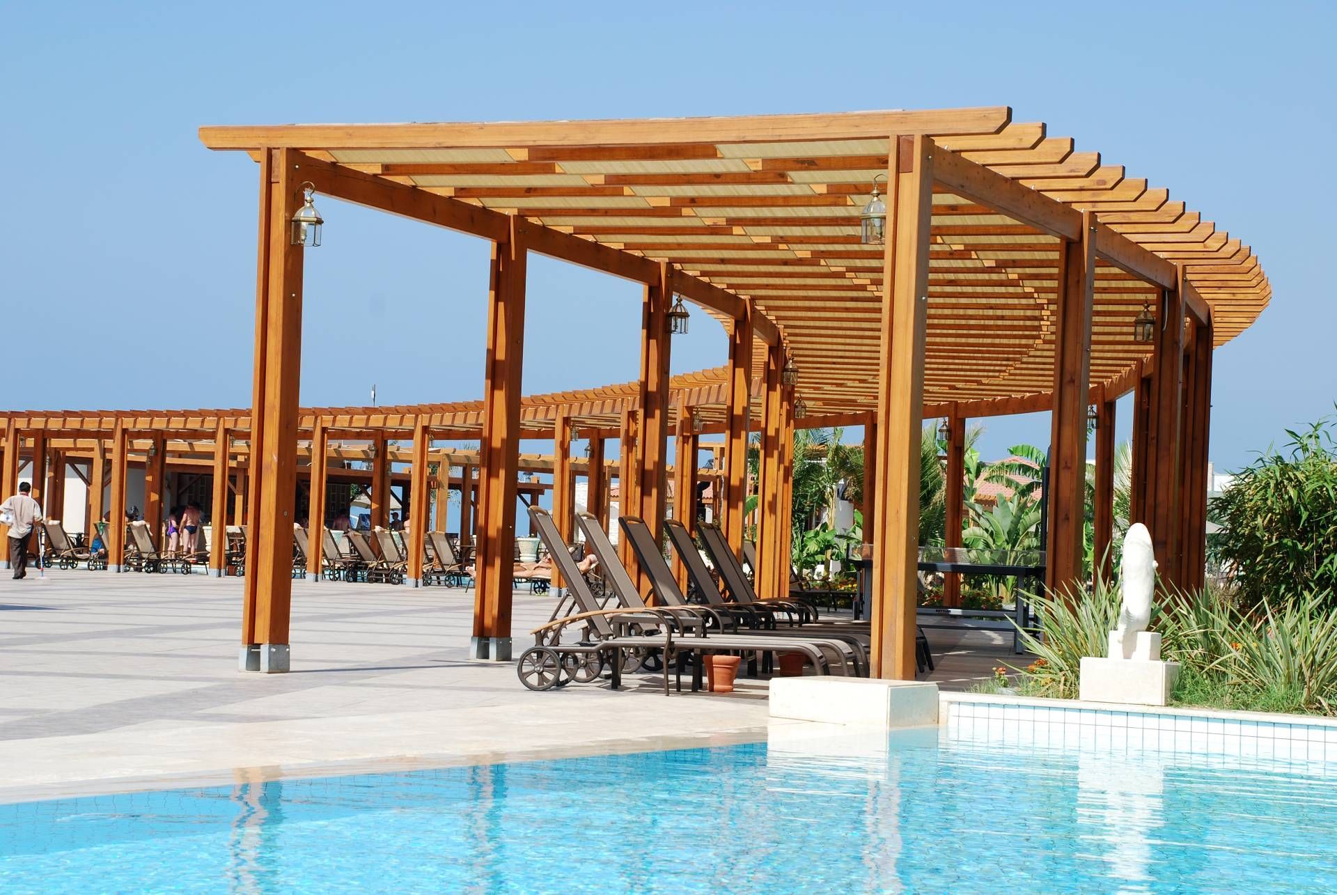 An outdoor commercial pergola, providing coverage to lounge chairs at a stunning hotel pool area nea