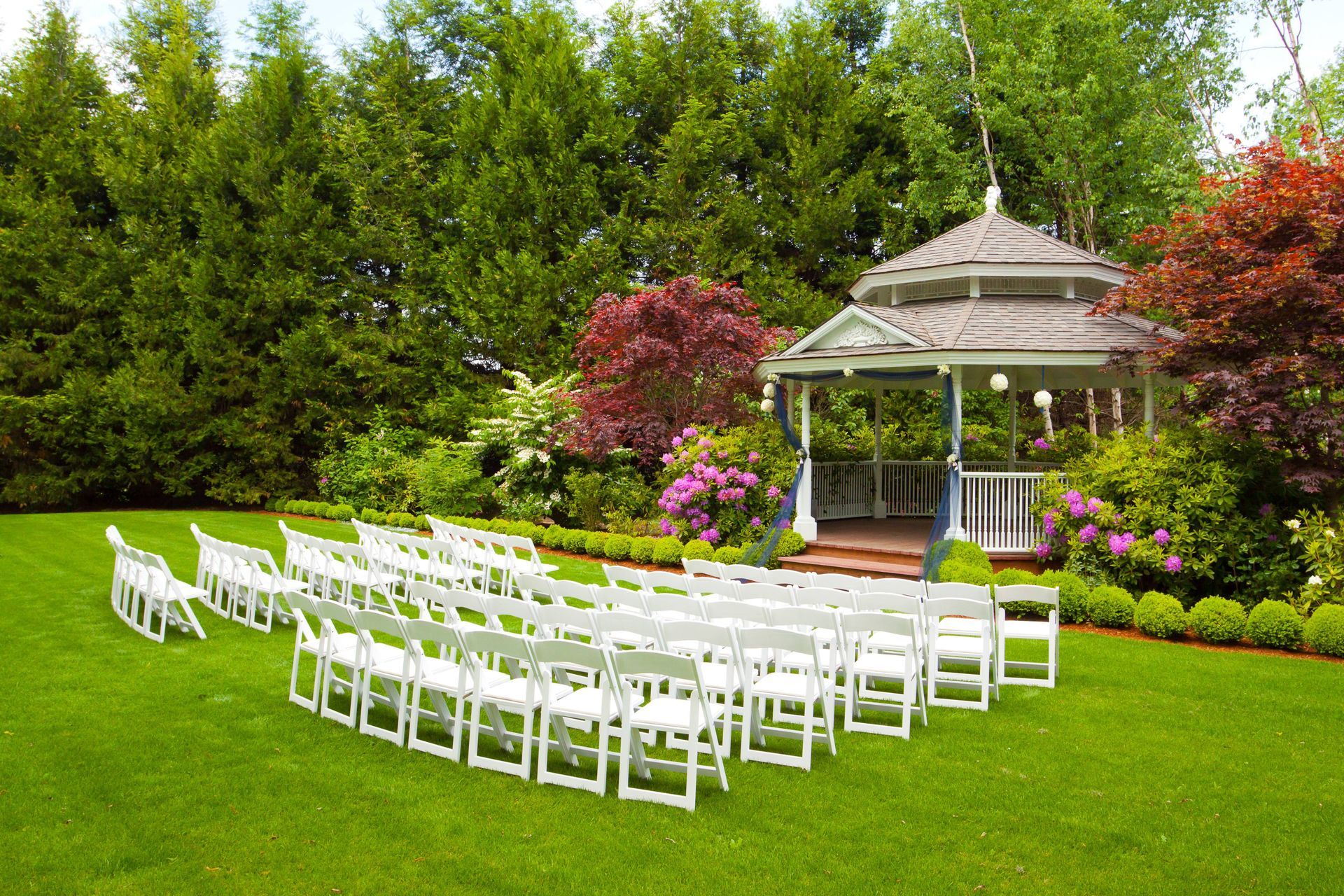 Gazebo wedding ceremony with white chairs, stunning florals, and lush greenery at a wedding venue at