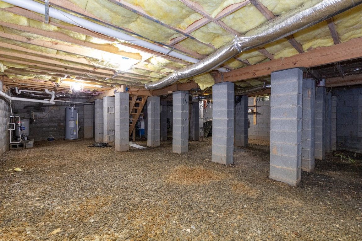 Basement with concrete block columns supporting wooden beams, gravel floor, insulation overhead.