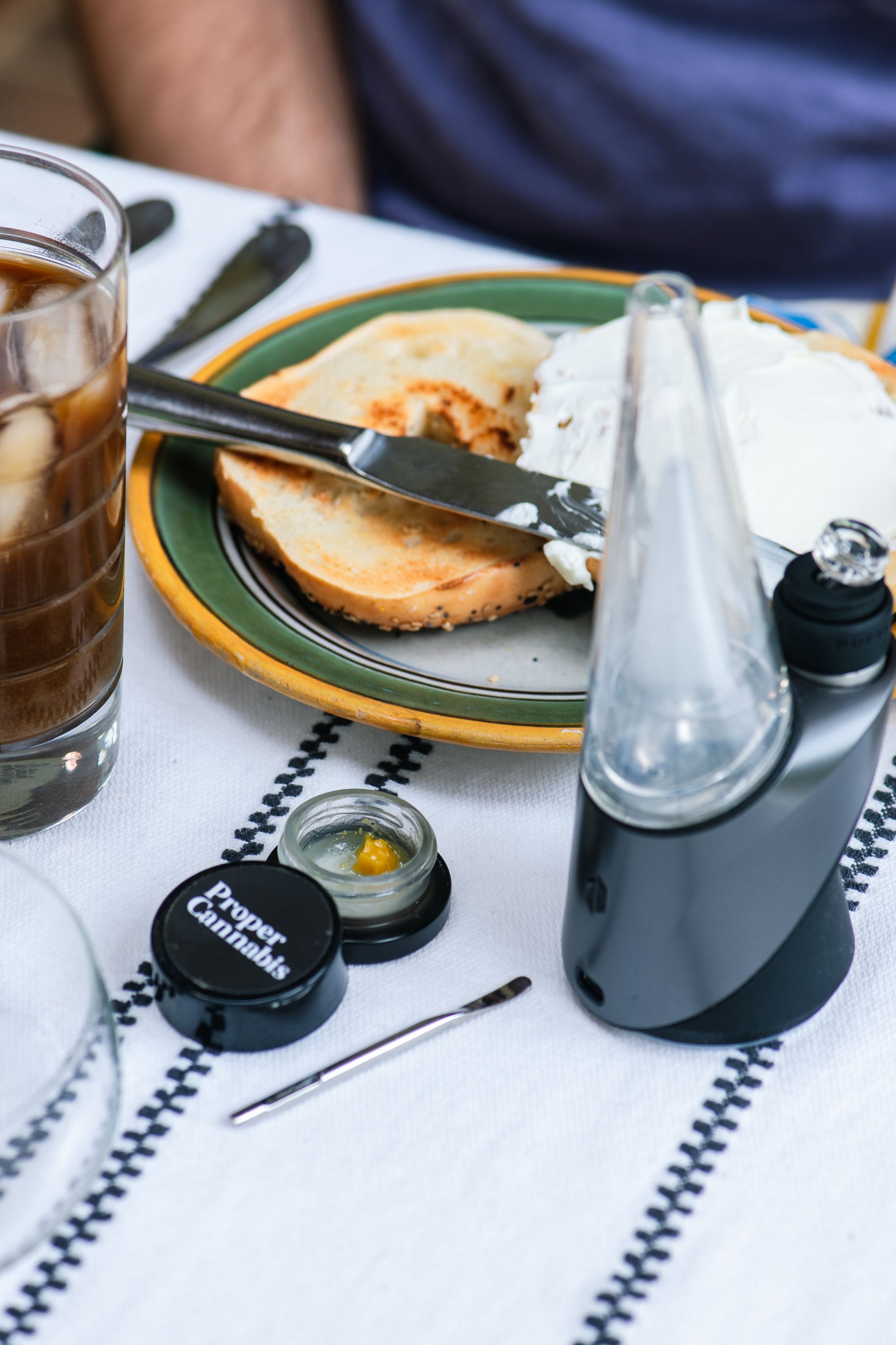 a table with a plate of food, a glass of coffee, a puffco, and gram of hash