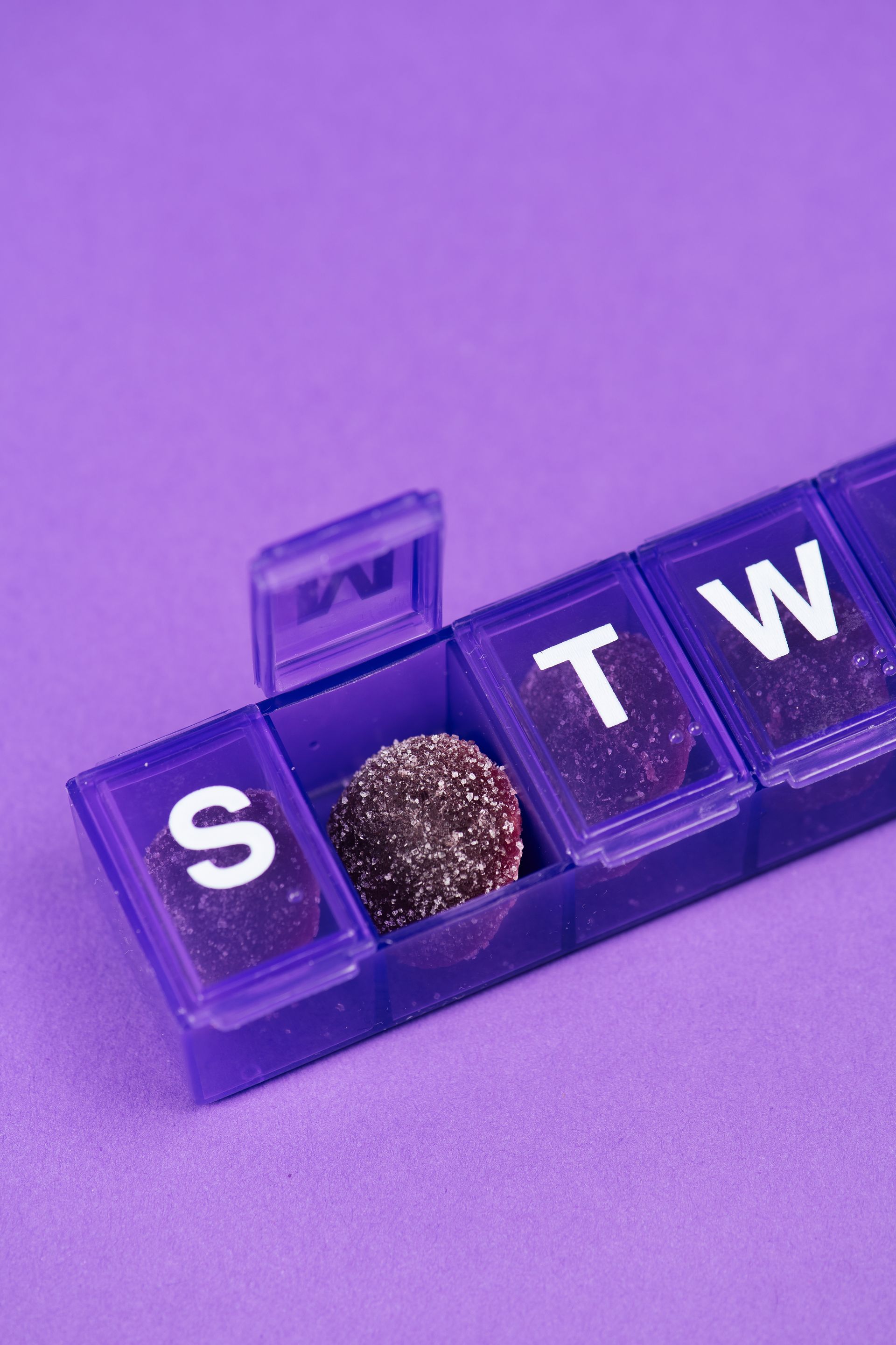 A purple pill holder with a gumdrop in it on a purple surface.