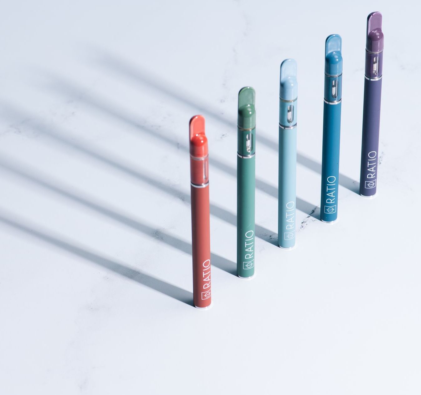 All 5 ratio vapes lined up on marble counter with harsh shadow behind