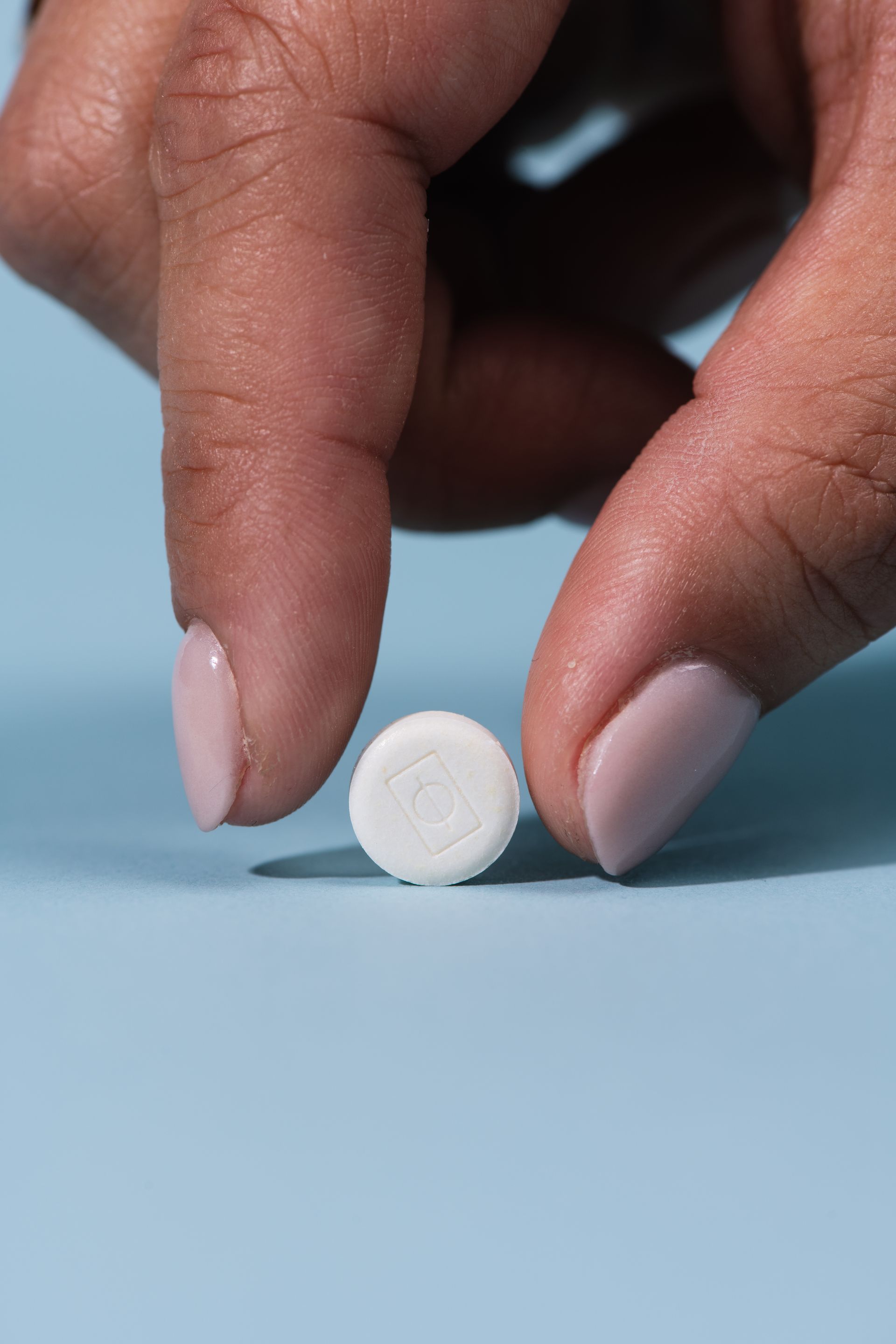 A small RATIO mint resting on blue background, soon to be picked up by woman