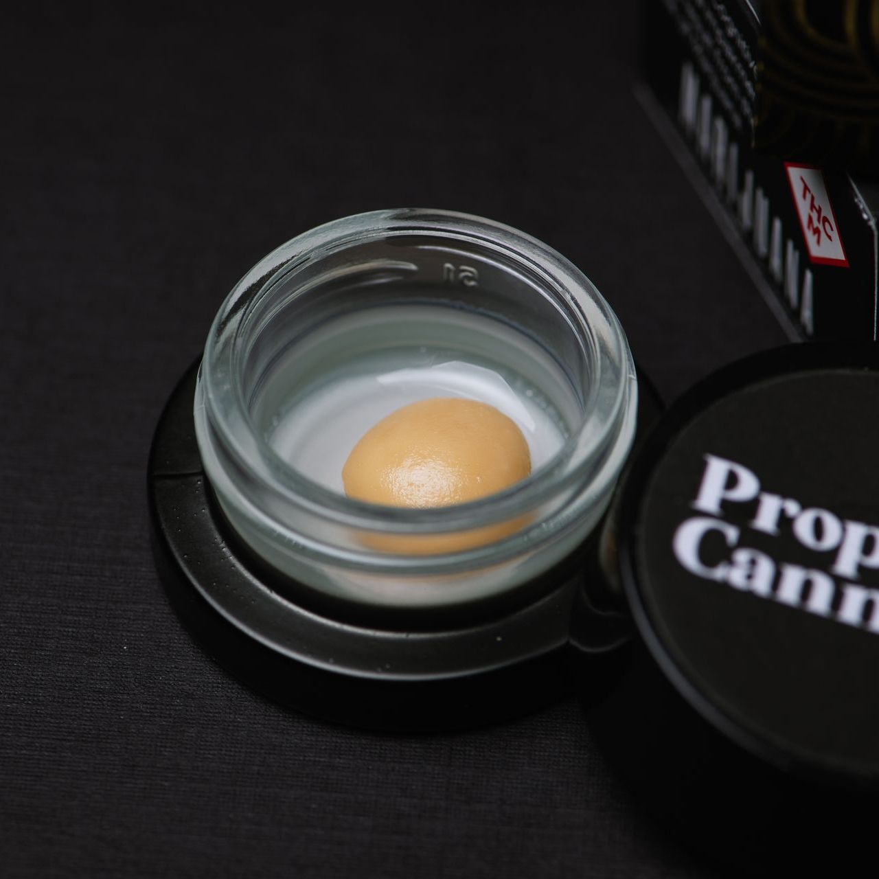 Gram of beige rosin in a concentrate jar on a black background.